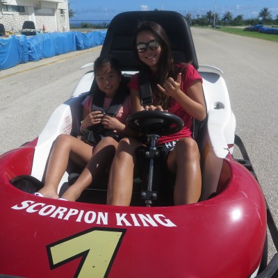 A woman and a young girl throw up hand signs while in a go kart