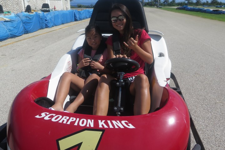 A woman and a young girl throw up hand signs while in a go kart