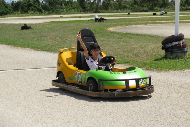 A kid giving the peace sign while driving a go kart