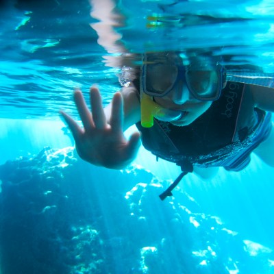A little girl waves at the camera as she is snorkeling