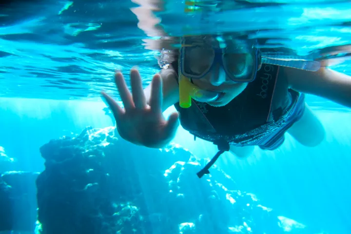 A little girl waves at the camera as she is snorkeling