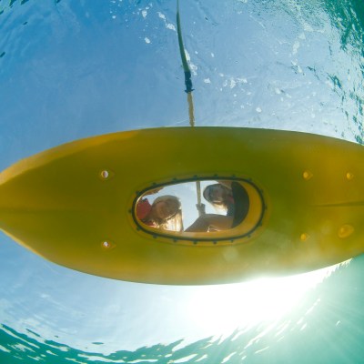 Two guests looking at a camera underwater through a clear panel on their kayak