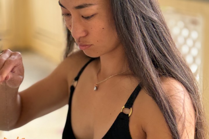 Woman in black top stringing orange flowers with a focused expression.